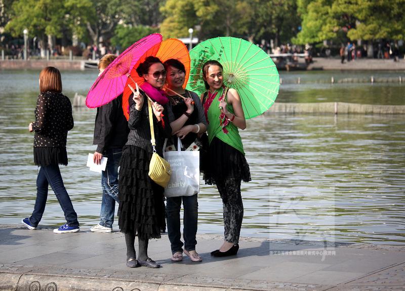 4月19日,西湖边的三位美女游客,分别打着红黄绿三色绸伞,开心地拍照